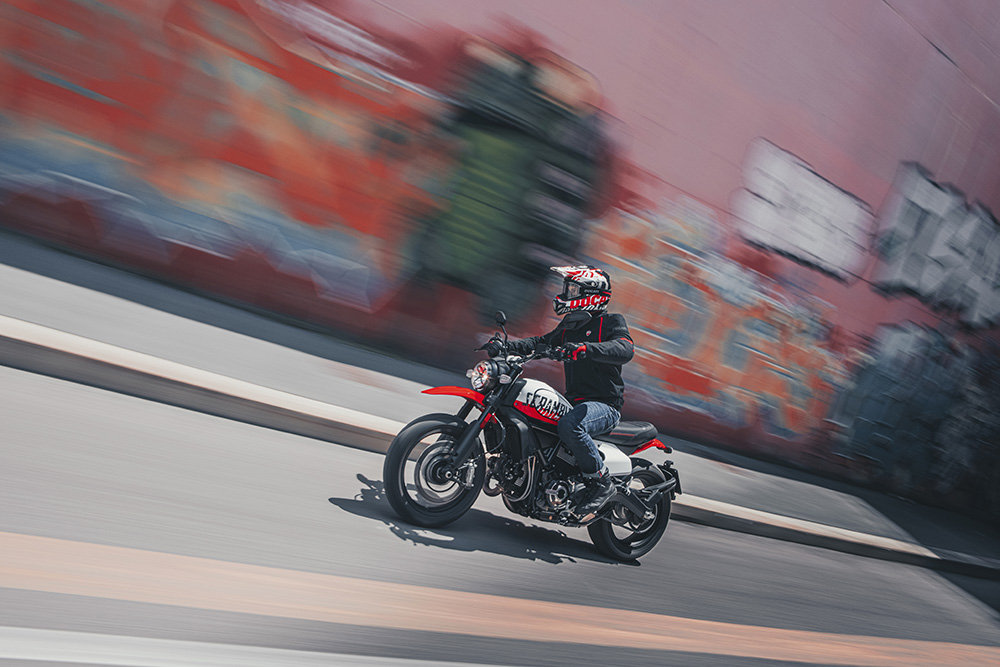 Motorcycle rider on Ducati Scrambler Urban Motard, moving at pace through the city.