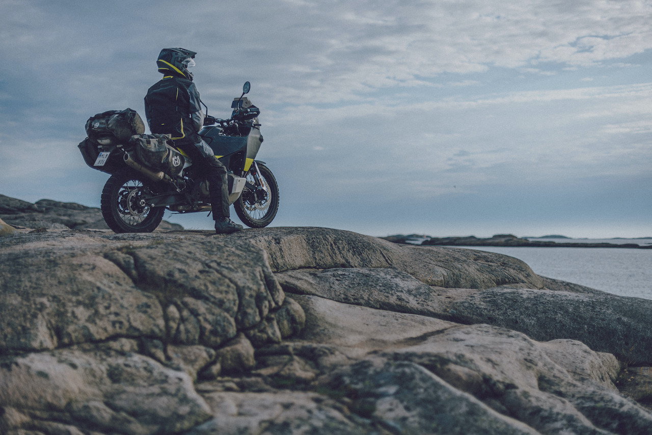 Rider sitting on Husqvarna Norden 901 on top of rocks looks out to sea